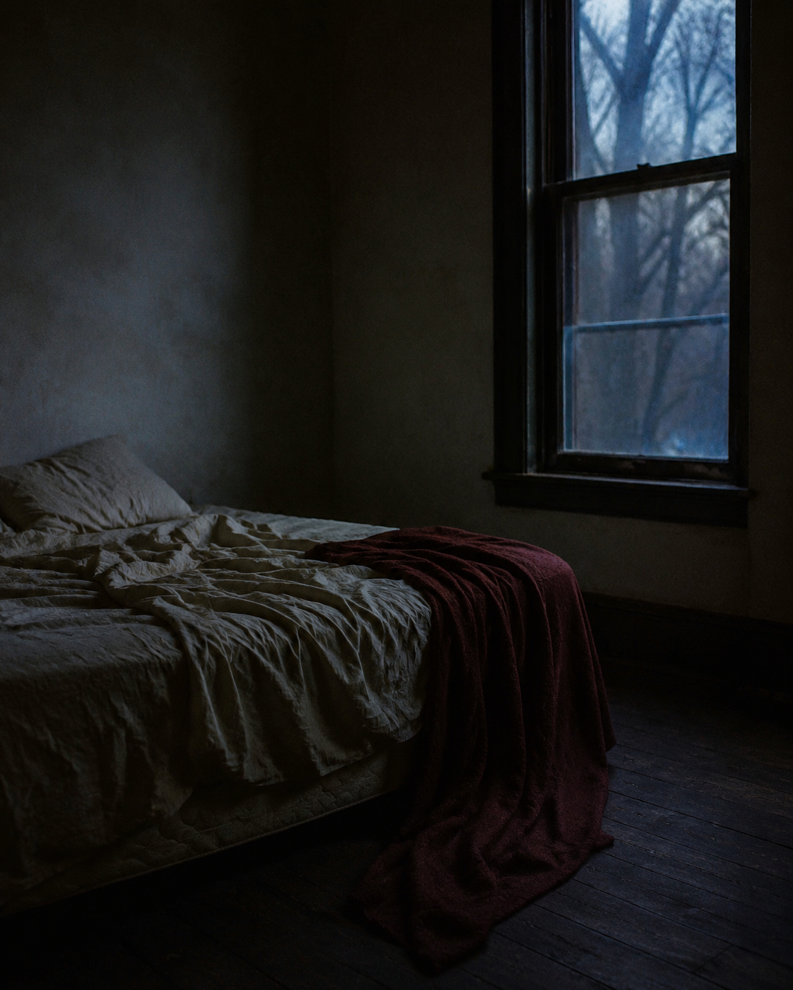 An unmade bed in a shadowed room before dawn